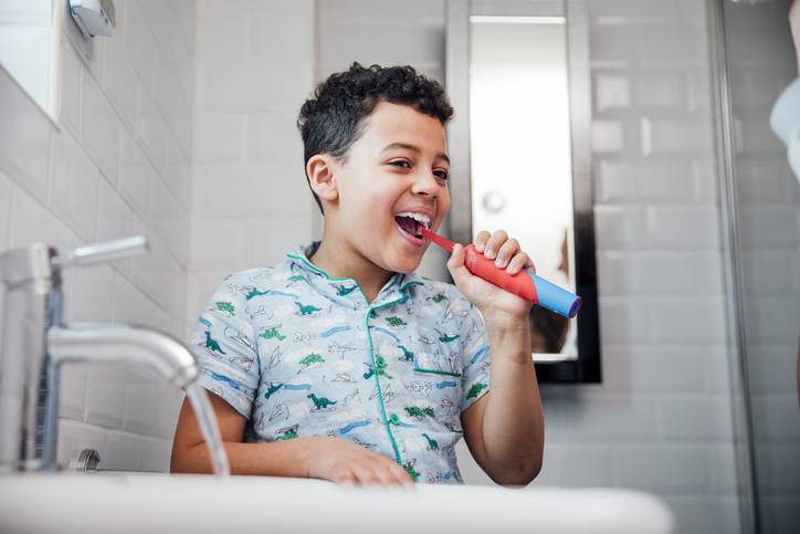 Photo of a child happily brushing his teeth with an electric toothbrush